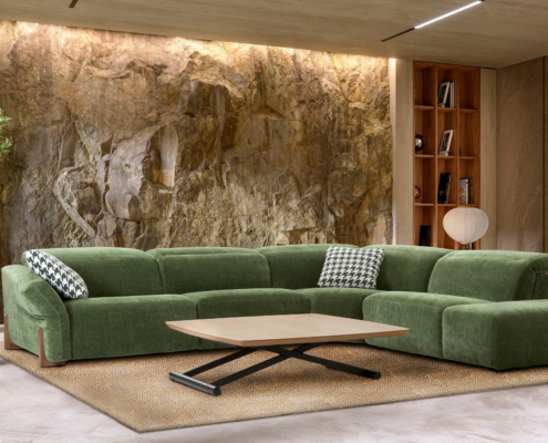 Render 3D de un salón moderno inundado de luz natural, con un sofá rinconera gris, cojines decorativos de color mostaza y estampados, una mesa de centro redonda negra y una lámpara de pie moderna, con vistas a un balcón.