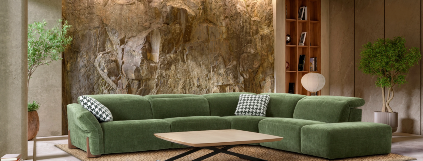 Render 3D de un salón moderno inundado de luz natural, con un sofá rinconera gris, cojines decorativos de color mostaza y estampados, una mesa de centro redonda negra y una lámpara de pie moderna, con vistas a un balcón.